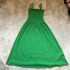 Grön sommarklänning med smock från H&M - Säljer en grön klänning från H&M med smock upptill och tunna axelband. Klänningen har en luftig passform och är perfekt för varma dagar. Enkel och stilren design som passar till många tillfällen. Hör av er vid frågor❤️