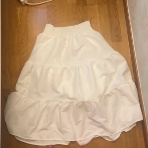 Vit volangkjol med resårmidja - Säljer en vit kjol med flera volanger och bred resår i midjan. Kjolen har en luftig och flowy känsla, perfekt för varma dagar. Passar dig som gillar en romantisk och enkel stil.