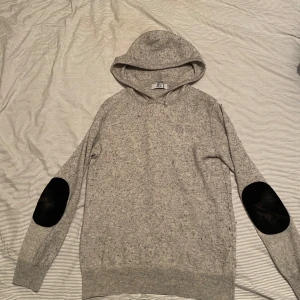 Bvaldi hoodie med svarta lappar  - Säljer en stilren Kashmir hoodie från Bvaldi med svarta armbågslappar. Tröjan har huva med dragsko och långa ärmar. Perfekt för en avslappnad och trendig look.