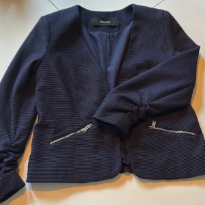 Mörkblå kavaj/tröja/vår jacka med dragkedjor från Vero Moda - Snygg mörkblå kavaj/tröja/vår jacka  från Vero Moda med ribbad struktur och två silvriga dragkedjor framtill. Jackan har trekvarts/långa ärmar med rynkade detaljer vid handlederna och en klassisk, öppen passform. Stl 36