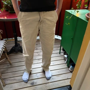 Beiga chinos från Stone Island - Säljer ett par beiga chinos från Stone Island med klassisk svartvit logotyp på bakfickan. Byxorna har normal passform, raka ben och stängs med dragkedja och knapp. Perfekta för en stilren och avslappnad look. Enda defekt är en liten fläck på sista bilden men syns inte vid andvändning. Pris kan självklart diskuteras och tveka inte vid att höra av er vid minsta fundering.