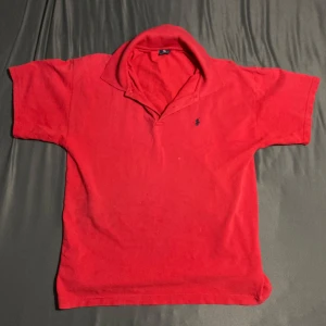 Röd pikétröja från Ralph Lauren - Säljer en klassisk röd pikétröja från Ralph Lauren i storlek XL. Tröjan har korta ärmar, krage och knäppning vid halsen samt den ikoniska broderade loggan på bröstet. Perfekt för en stilren och avslappnad look. Riktigt bra små defekter  (de sista bild) riktigt fin. Defekterna påverkar ej! 
