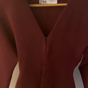 Vinröd topp med v-ringning från Zara - Säljer en vinröd topp från Zara med v-ringad hals och lång ärm. Toppen har en figurnära passform och är perfekt för dig som gillar stilrena plagg med enkel design.