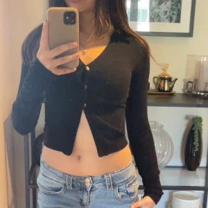 Svart croppad kofta med v-ringning - Säljer en svart, croppad kofta med v-ringning och knappar framtill. Tröjan är ribbad och har långa ärmar, perfekt för en trendig och stilren look. Passar dig som gillar en tight passform och vill ha något enkelt men snyggt! Storlek XXS men passar som XS också, använt bara en gång 💕
