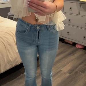 Ljusblå bootcut jeans med detaljerade bakfickor - Säljer ett par ljusblå jeans med bootcut-modell och snygga detaljer på bakfickorna. Jeansen har normal passform, klassisk femficksdesign och stängs med dragkedja och knapp. Perfekta för dig som gillar en tidlös look.