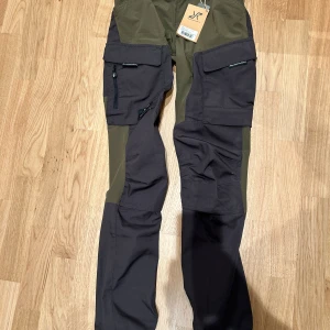 Grön-svarta friluftsbyxor från RevolutionRace - Säljer ett par grön-svarta friluftsbyxor från RevolutionRace, modell GPX Pants Women. Byxorna har flera praktiska fickor med dragkedja och förstärkta partier på knän och bak. Perfekta för utomhusaktiviteter och äventyr.