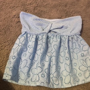 Ljusblå kjol med virkad midja och broderade blommor - Supersöt ljusblå kjol med bred, virkad midja och broderade blommor på kjoldelen. Kjolen är kort och har en luftig känsla, perfekt för varma dagar. Midjan är elastisk och sitter bekvämt.