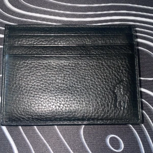 Svart korthållare från Polo Ralph Lauren - Säljer en stilren svart korthållare i skinn från Polo Ralph Lauren. Korthållaren har flera kortfack och är prydd med både logotyp och den klassiska häst-symbolen. Perfekt för dig som vill ha en smidig och snygg plånbok i vardagen. 