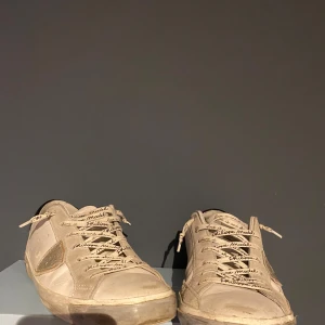 Beige sneakers från Philippe Model - Säljer ett par beige sneakers från Philippe Model med snörning och paneler i mocka och skinn. Skorna har rund tå och platt sula, samt märkets logga på sidan. Perfekta för dig som gillar stilrena och klassiska sneakers.