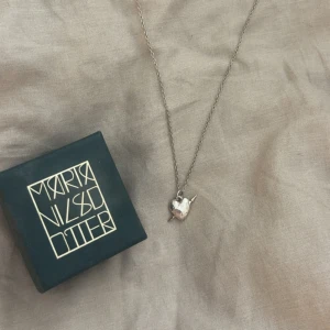  halsband från Maria Nilsdotter - Säljer ett stilrent halsband i silverfärg från Maria Nilsdotter. Hänget är format som ett hjärta med en liten pil genom, vilket ger en unik och cool detalj. Perfekt för dig som gillar personliga smycken. Jättebra skick, längd 40💕har ej kvitto kvar 