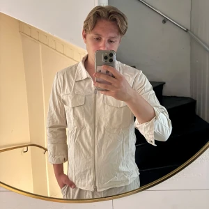Vit overshirt från Bläck - Säljer en stilren vit overshirt från Bläck med klassisk krage och två bröstfickor med lock. Jackan har dragkedja framtill och är långärmad. Perfekt för lager-på-lager och enkel att matcha.