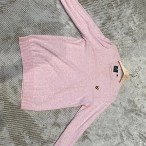 Ljusrosa stickad tröja från Lyle & Scott - Säljer en ljusrosa stickad tröja från Lyle & Scott med deras klassiska gula logga på bröstet. Tröjan har rund halsringning och långa ärmar. Perfekt för en stilren och avslappnad look.