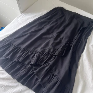 Svart volangkjol från Lindex - Säljer en svart kjol från Lindex med volangdetaljer nertill. Kjolen har en normal passform och resår i midjan för extra komfort. Perfekt att styla med en stickad tröja eller t-shirt. Säljer pågrund av att den är för liten! Väldigt fint skick