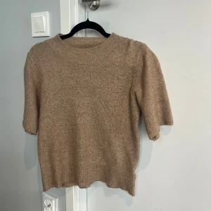 Beige stickad t-shirt - Mysig beige stickad t-shirt från By Swan med rund halsringning och kortare ärmar. Tröjan har en enkel och stilren design med ribbade muddar vid hals, ärmslut och nederkant. Skicka gärna till mig vid vidare frågor😊🫶🩷