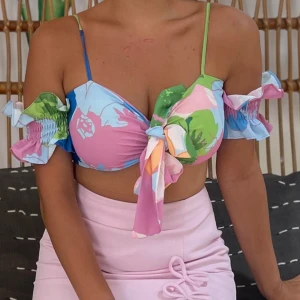 Blus - Säljer en superfin croppad blus med färgglatti blommigt mönster i rosa, blått och grönt. Toppen har offshoulder-ärmar med volangdetaljer och knyt framtill. Perfekt för sommardagar och festivaler!