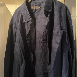 Mörkblå skjorta från Dressman (storlek xxl) - Säljer en klassisk mörkblå skjorta från Dressmann. Skjortan har lång ärm, knappar framtill och en bröstficka. Perfekt för dig som gillar en stilren och enkel look.