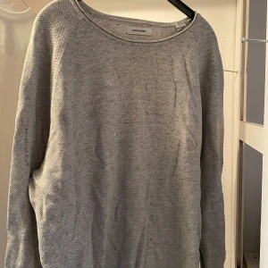 Ljusgrå stickad tröja från Jack & Jones - En enkel och stilren ljusgrå stickad tröja från Jack & Jones. Tröjan har rund halsringning och långa ärmar, perfekt för lager-på-lager under kyligare dagar.