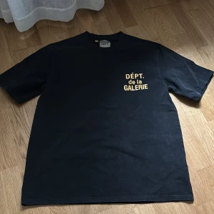 Svart t-shirt från Gallery Dept. - Svart t-shirt från Gallery Dept. med gul text 'DÉPT. de la GALERIE' tryckt på bröstet och i större format på ryggen. Klassisk passform och rund halsringning. Tillverkad i 100% bomull för en skön känsla. Den är även helt oanvänd. Vill inte ha den eftersom den är inte i min storlek. ⚠️1:1⚠️