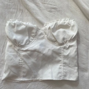 Vit tubtopp korsett - Säljer en vit axelbandslös korsett-topp med markerade kupor och figurnära passform. 