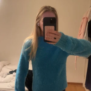 Blå fluffig stickad tröja - Supermysig blå stickad tröja med fluffig känsla och rund hals. Långärmad modell med relaxed fit, perfekt för kyliga dagar. Enkel och stilren design som är lätt att matcha med jeans eller kjol.