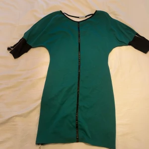 Grön kortklänning med svarta detaljer - Säljer en grön kortklänning med svarta ärmar och dragkedjor både på ärmar och nertill. Storlek 44