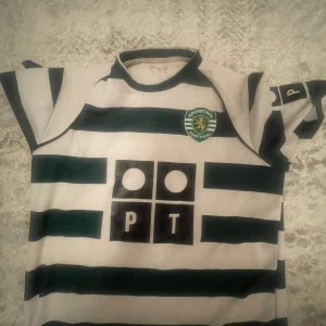 Sporting Lissabon Ronaldo tröja Reebok - Klassisk Sporting Lissabon fotbollströja med gröna och vita ränder, C. Ronaldo och nummer 28 på ryggen. Märkt med klubbens emblem och sponsortryck på bröstet. Kortärmad modell i lätt och ventilerande material, perfekt för fotbollsälskare.