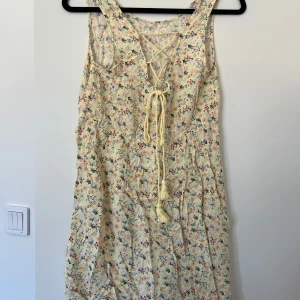 Blommig sommarklänning med snörning - Söt blommig kortklänning i ljusgul ton med små blommor i rosa, blått och grönt.