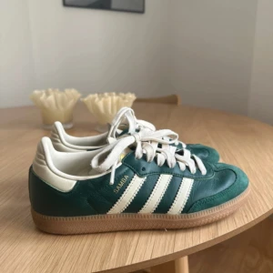 Adidas Samba gröna sneakers - Säljer ett par klassiska Adidas Samba sneakers i grönt och vitt med de ikoniska tre ränderna på sidan. Skorna har snörning, gummisula och ovandel i skinn och mocka. Perfekta för dig som gillar retrostil och streetwear. Endast använda 4 gånger! 