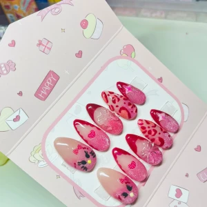 Rosa och röda press-on naglar kawaii - Säljer ett set med 10 st press-on naglar i mandelform med olika rosa och röda designer. Naglarna har glitter, hjärtan, rosetter, leopardmönster och söta kattmotiv. Perfekt för dig som älskar kawaii och vill ha unika naglar med mycket detaljer.