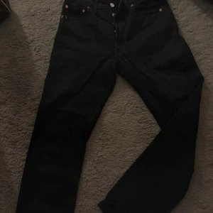 Svarta Levi's 501 jeans straight fit - Klassiska svarta Levi's 501 jeans i 100% bomull. Modellen har raka ben, knappgylf och fem fickor. Snygg och tidlös passform som funkar till allt. Ikonisk läderpatch bak och röd Levi's-tagg på bakfickan. Skriv gärna för fler bilder. PRIS KAN DISKUTERAS!!🥰