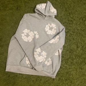Grå denim tears hoodie - Grå Denim Tears hoodie med högkvalite, oversized hoodie med ikoniska tryck som hyllar afroamerikansk historia. Den kombinerar kultur och statement med modern streetwear och är populär bland kända profiler. Limitert släpp gör den eftertraktad och den håller länge med snygg vintage-känsla