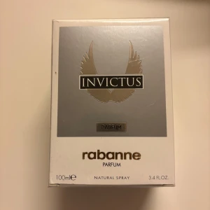Invictus Parfum 100ml från Rabanne - Invictus Parfum från Rabanne i en snygg silver- och vit förpackning med guldiga detaljer. Flaskan rymmer 100 ml och är en naturlig spray. Designen har en modern känsla med vingar på framsidan och stilren logotyp. Perfekt för dig som gillar exklusiva dofter. Helt ny och oöppnad 