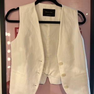 Vit linneväst från Massimo Dutti - Stilren vit väst i linne från Massimo Dutti med klassisk passform. Västen har tre knappar framtill, två fickor och en snyggt skuren nederkant baktill. Perfekt att styla över en skjorta för en clean och fräsch look.