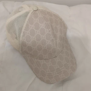 Gucci keps  - Snygg beige från Gucci med klassiskt GG-monogram över hela kepsen. Baksidan är i mesh för extra ventilation och justerbar rem i läder med gulddetalj. Perfekt accessoar för en trendig look.