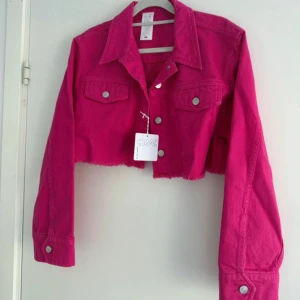 Croppad rosa jeansjacka från Carin Wester - Trendig croppad jeansjacka i stark rosa från Carin Wester. Jackan har rå kant nertill, klassisk krage, bröstfickor med knappar och långa ärmar. Perfekt för dig som vill sticka ut med färg och cool passform. Nypris : 799kr