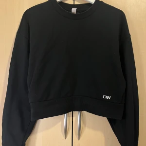 Svart croppad sweatshirt från ICANIWILL - Svart croppad sweatshirt från ICANIWILL med broderad vit logga framtill. Tröjan har långa ärmar, ribbade muddar och bred ribbad kant nedtill. Perfekt för en chill och sportig look. Mjuk bomullskänsla och relaxed fit.