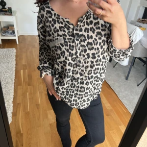 Leopardmönstrad blus med glitterdetaljer - Snygg henley-blus med leopardmönste. Skjortan har coola glittriga detaljer på bröstfickan och längs ärmarna. Storlek S/M, fint skick! 