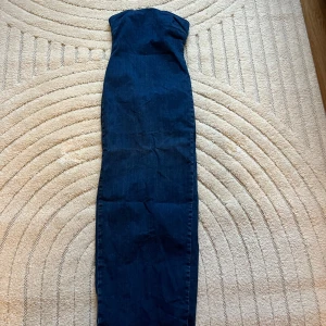 Mörkblå lång jeans klänning med rå kant - Säljer en lång, mörkblå jeans klänning med tight passform och rå, fransig kant nertill. Klänningen har klassisk denimlook. Dragkedja baktill och söm på bysten. 