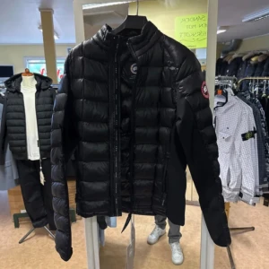 Svart dunjacka från Canada Goose - Snygg svart dunjacka från Canada Goose med klassisk logga på ärmen. Jackan har quiltad design, dragkedja framtill och hög krage. Perfekt för kalla dagar och riktigt stilren att bära till det mesta. Lätt och smidig modell som ändå håller värmen.