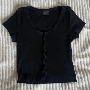 Svart croppad topp från Gina Tricot - Svart croppad topp från Gina Tricot med korta ärmar och djup och knappar som går att öppna. Har endast använts 2-3 gånger men är verkligen en jättegullig top som går att stylea med allt💗