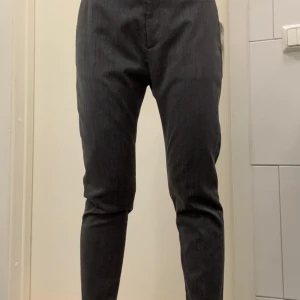 Grå kostymbyxor från HOPE - Snygga grå kostymbyxor från HOPE med diskret mönster och smal passform. Byxorna har hällor för bälte och klassisk design, perfekta för en clean och stilren look. Materialet känns mjukt och har en lätt struktur.