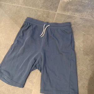 Blå shorts med snörning från H&M - Snygga blå shorts från H&M med elastisk midja och vit snörning framtill. Tillverkade i mjuk bomullsmix som känns skön mot huden. Perfekta för sommardagar eller chill hemma. Klassisk passform och enkel stil som funkar till det mesta.