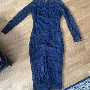 Marinblå spetsklänning med slits - Snygg marinblå långklänning i spets med lång ärm och figurnära passform. Klänningen har ett vackert spetsmönster över hela tyget och en slits bak för extra rörelsefrihet. Perfekt för dig som vill sticka ut med en elegant look. Storlek S-M
