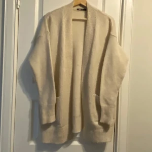 Beige kofta från Gina Tricot! -  Fint skick! Mysig lite längre  beige kofta från Gina Tricot i storlek S. Den är stickad, har långa ärmar, två stora fickor framtill och bred ribbad kant längs öppningen och ärmsluten. Perfekt att slänga på sig över en t-shirt eller topp för en chill look. Är i mycket fint skick! Den är 80 cm lång. Ge gärna prisförslag, fler bilder finns! 