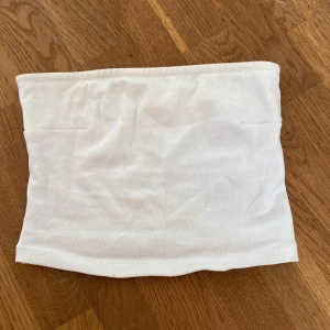 Vit bandeautopp  - En enkel och stilren vit bandeau tubtopp från Gina Tricot. Toppen är ribbad och ärmlös, perfekt för varma dagar eller som lager under andra plagg. Mjuk och stretchig bomullskänsla som sitter skönt mot kroppen. Finns endast en defekt som sitter i sömmen på ena sidan av toppen (se bild 4)💞