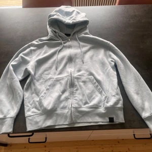 Ljusgrå hoodie från Pull&Bear - Snygg ljusgrå hoodie från Pull&Bear i storlek S. Tröjan har dragkedja framtill, huva med snörning och två stora fickor. Perfekt för chill dagar och enkel att matcha med jeans eller joggers.