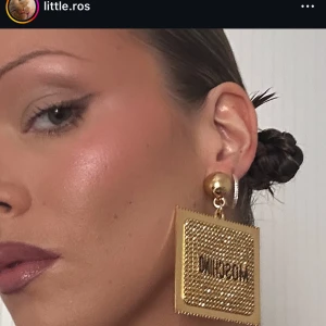 Guldiga kondom örhängen Moschino - Stora fyrkantiga örhängen från Moschino i guldigt metallmaterial med glittriga stenar och tydlig logga framtill. Klämfäste och cool retrovibe, perfekta för dig som vill sticka ut. Riktigt iögonfallande accessoar med lyxig känsla.