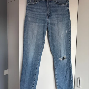 Ljusblå jeans från ONLY med slitning - Säljer ett par ljusblå jeans från ONLY med klassisk femficksmodell och slitning på ena knät. Jeansen har medelhög midja och raka ben, tillverkade i bomullsdenim. Sitter tightare runt låren och går sedan rakt ned vid vaderna. Är mjuka och bekväma och har en allmän ”loose” fit.