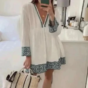 Vit kortklänning med grön mönster - Superfin vit kortklänning med v-ringning och långa ärmar. Klänningen har grönt mönster längs ärmslut, nederkant och ringning som ger en bohemisk vibe. Luftig och flowy passform, perfekt för varma dagar. Materialet känns lätt och svalt. Storlek M (L)