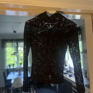 Svart spetsblus från Whyred XS - Supersnygg svart spetsblus från Whyred i storlek XS. Blusen har lång ärm, hög hals och har blommigt spetsmönster. Perfekt för dig som vill sticka ut med en elegant och trendig look. Dragkedja bak för enkel påklädning.